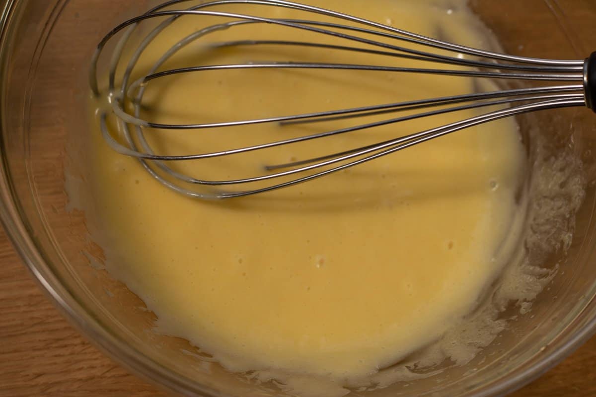 Mayonnaise at early stage of mixing in glass bowl with balloon whisk.