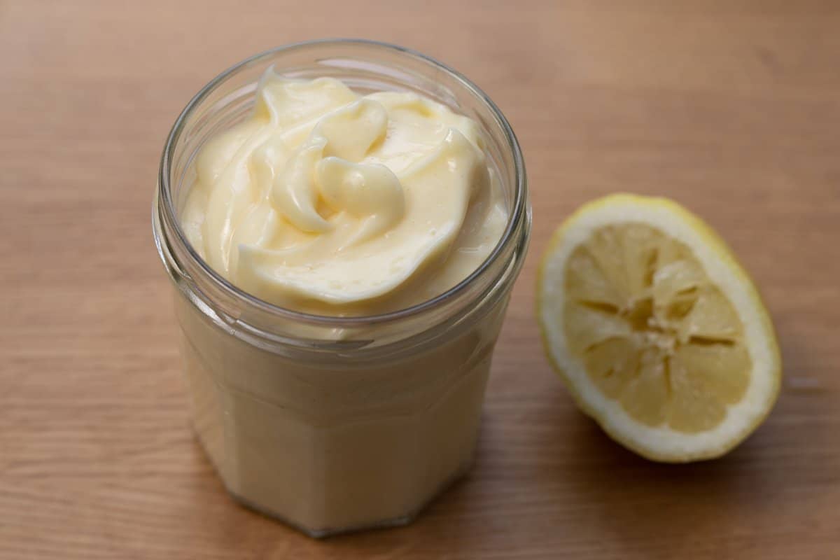 Mayonnaise in a glass jar beside squeezed lemon half.