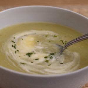 Leek and potato soup, with cream and chives, in a white bowl. A spoon is in the bowl.