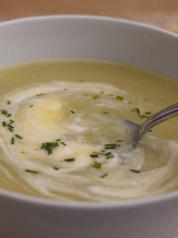 Leek and potato soup, with cream and chives, in a white bowl. A spoon is in the bowl.