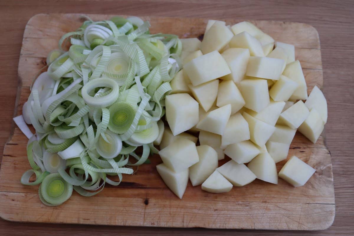 Sliced leeks and chopped potatoes on a wooden board.