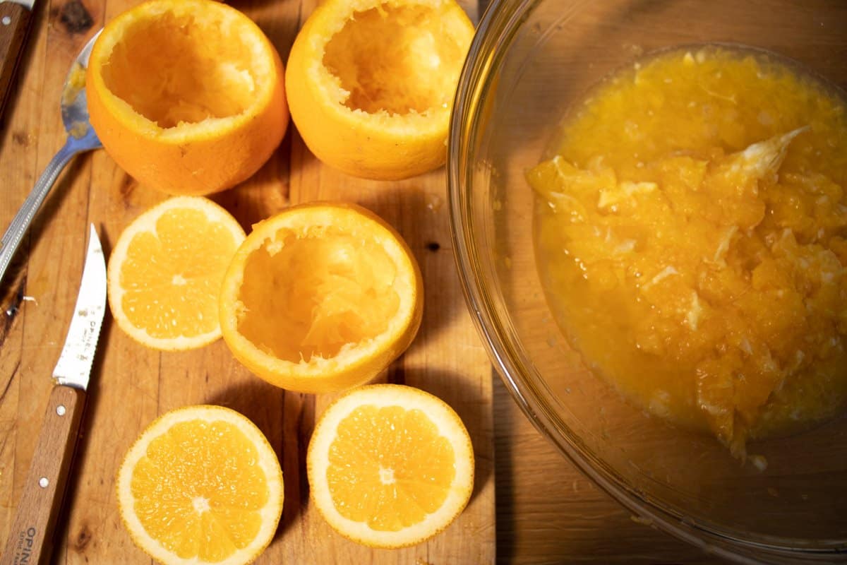 oranges with tops sliced off next to bowl containing orange pulp