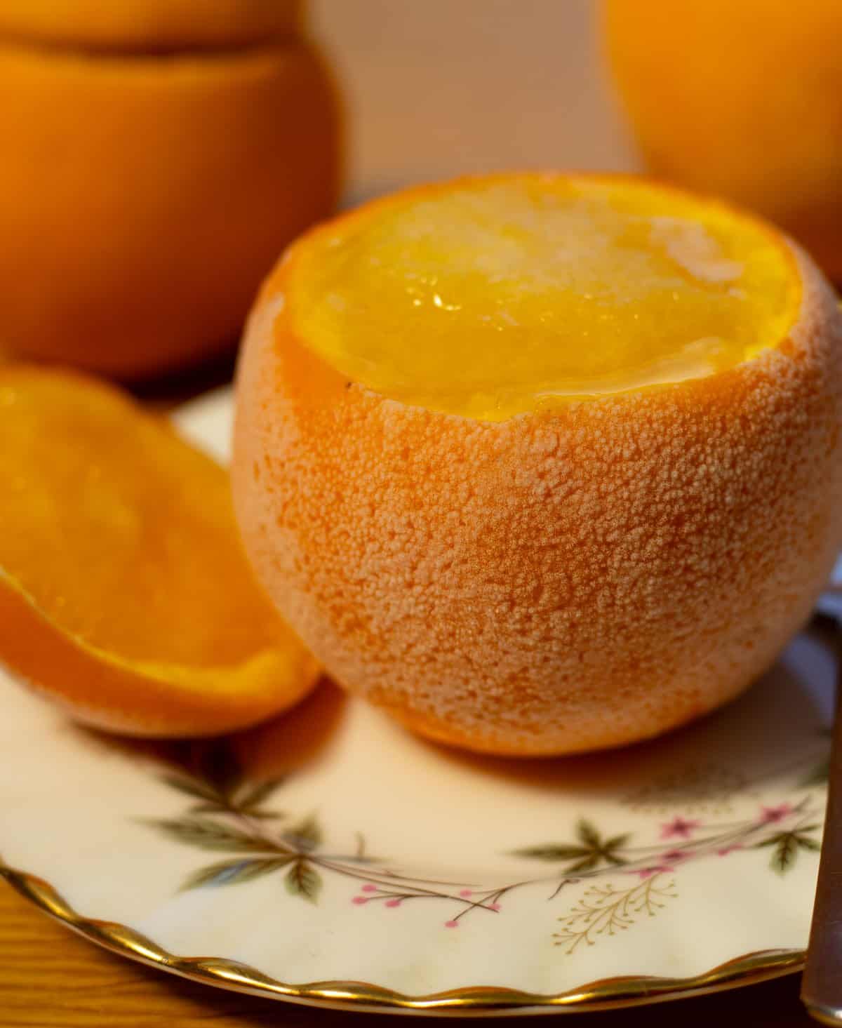 frozen orange containing orange sorbet on a plate next to frozen sliced off orange top