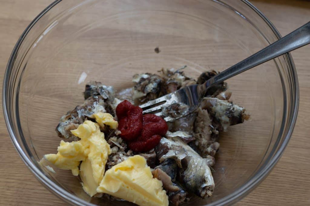 Tinned sardines, butter and tomato puree placed in a bowl with a fork ready for mixing together.