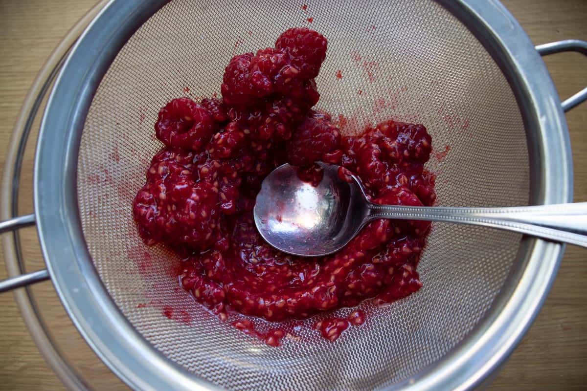 Crushed raspberries in wire sieve.