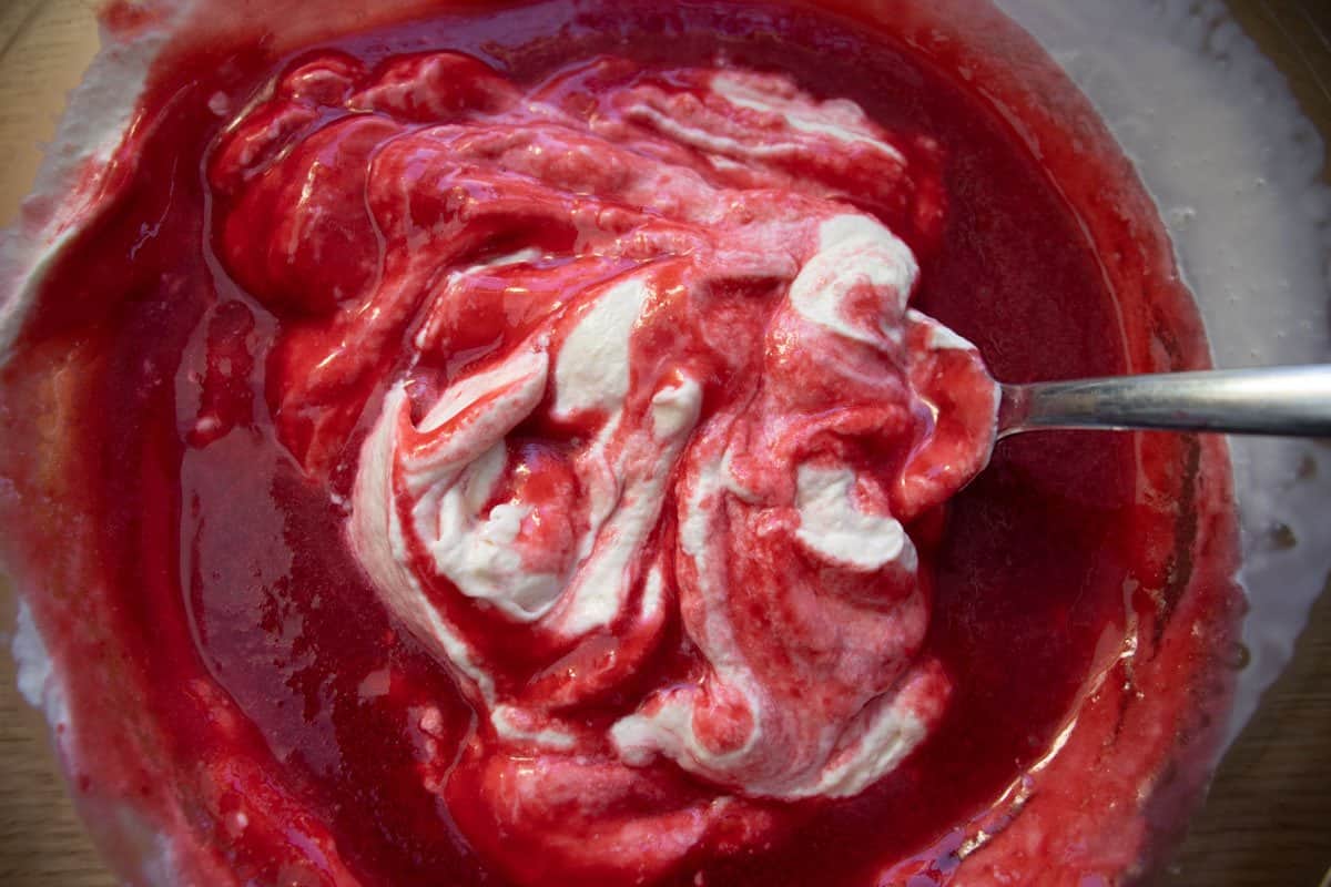 Raspberry coulis being mixed with cream in a glass bowl.