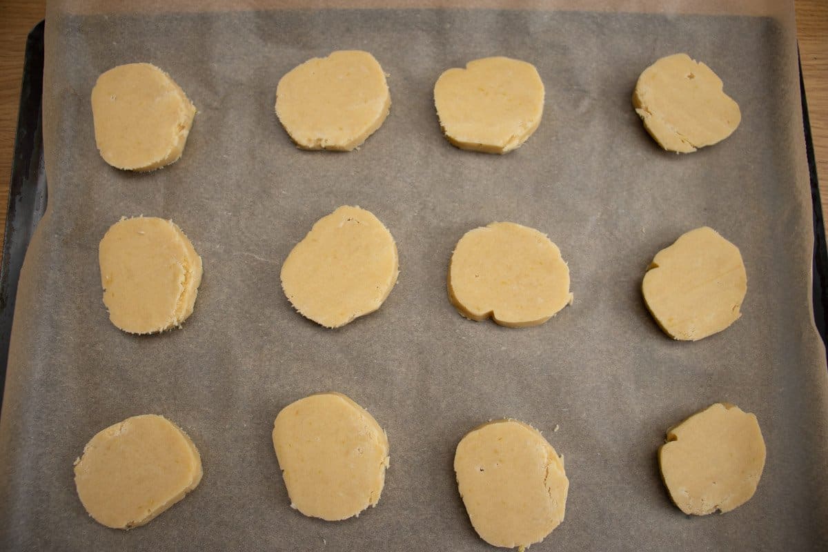 Uncooked lemon butter biscuits on greaseproof paper on baking tray