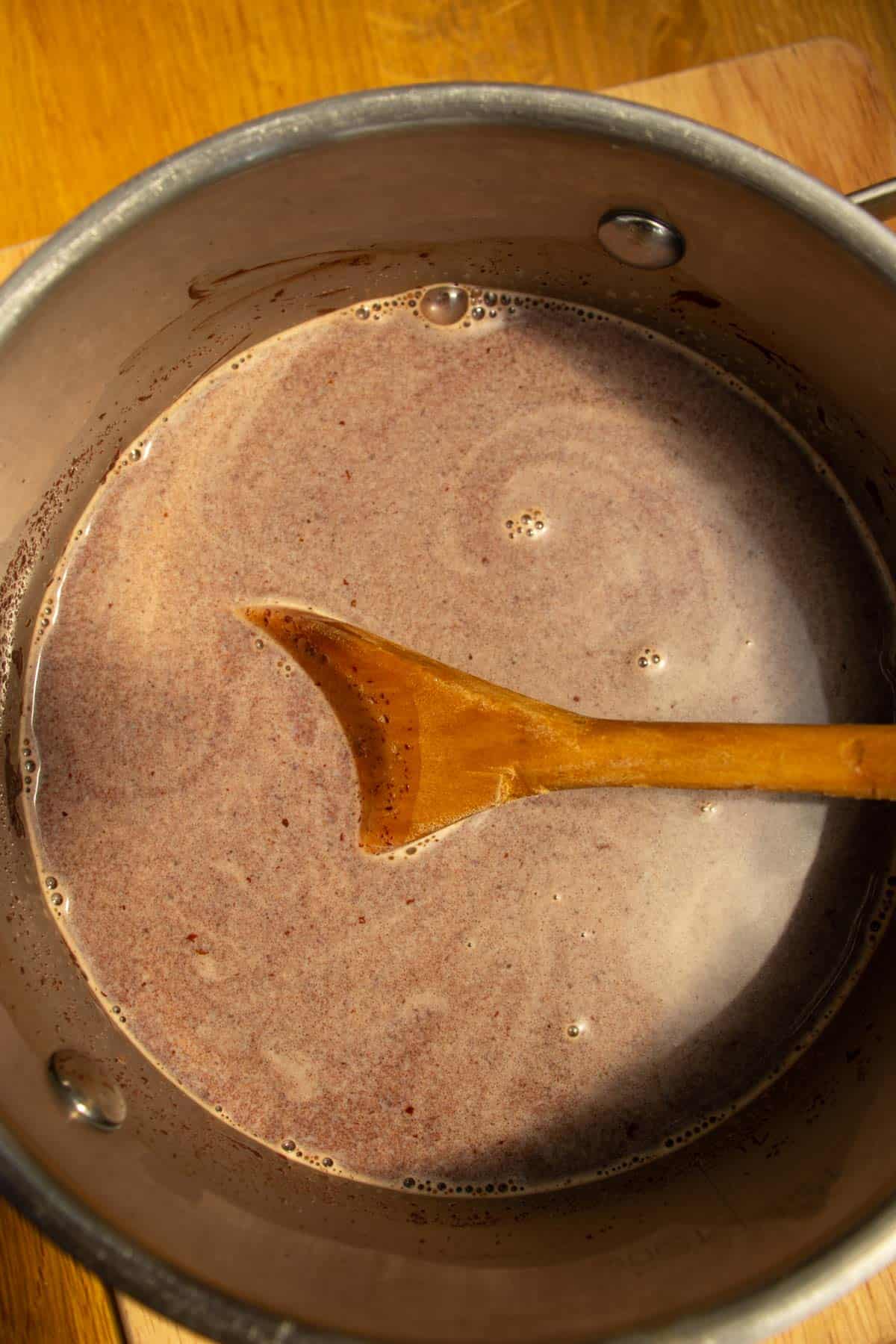 Chocolate Cremeux liquid mixture in a saucepan being stirred with a wooden spoon.