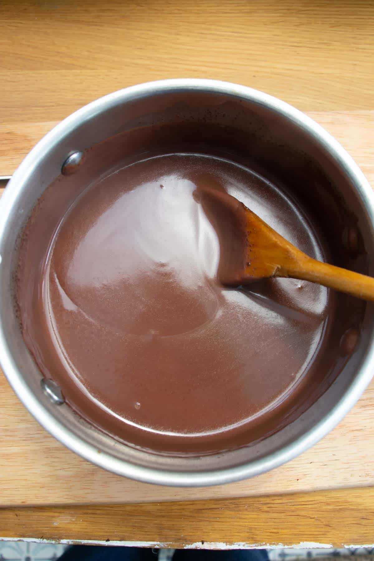 Glossy thick cremeux pudding mixture in a saucepan being stirred with a wooden spoon.