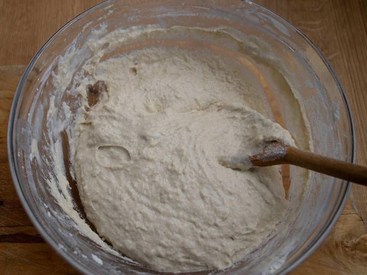 Nokedli dough mixture in glass bowl being stirred by wooden spoon.