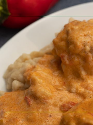 Paprika chicken and nokedli on white plate with red pepper in background