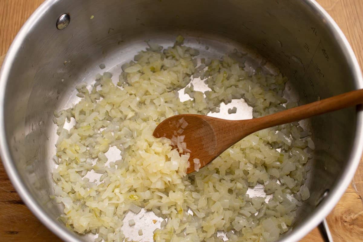 chopped onion frying in a saucepan and being stirred with a wooden spoon