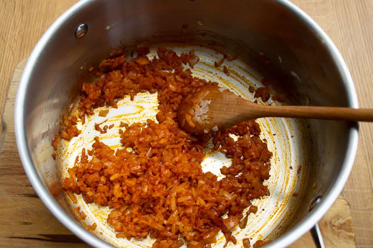 onion and paprika spice being stirred together in a saucepan with a wooden spoon