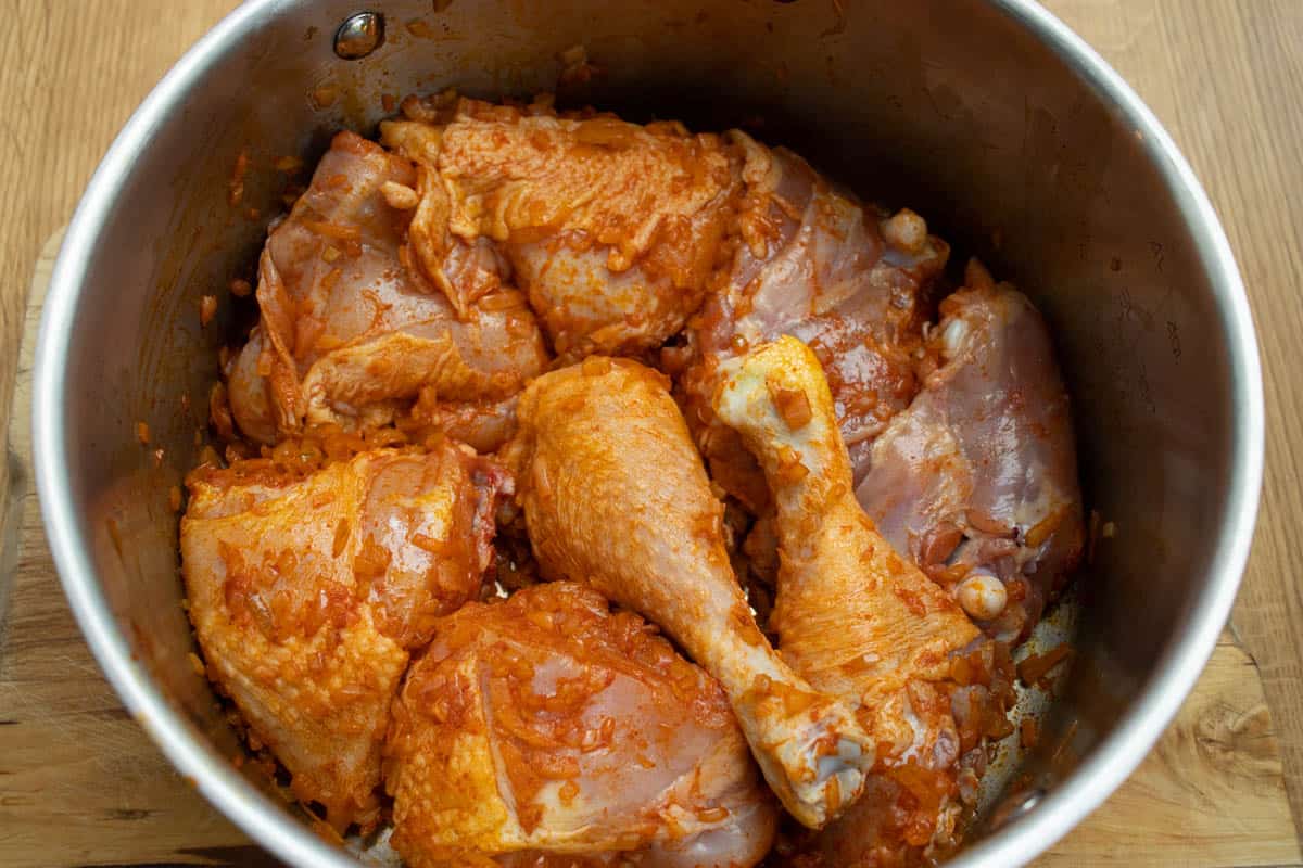 raw chicken pieces mixed with onion and ground paprika spice in a saucepan