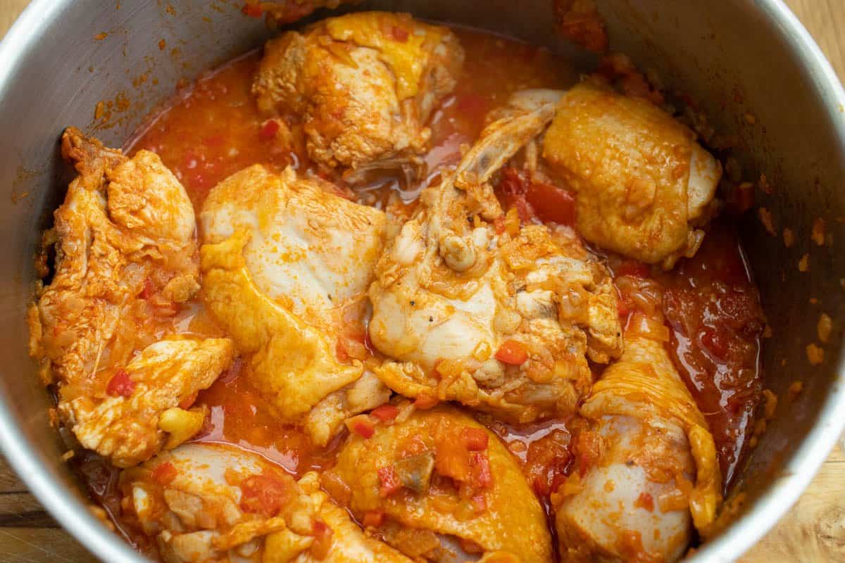 chicken pieces in paprika sauce with pieces of tomatoes and pepper in a saucepan