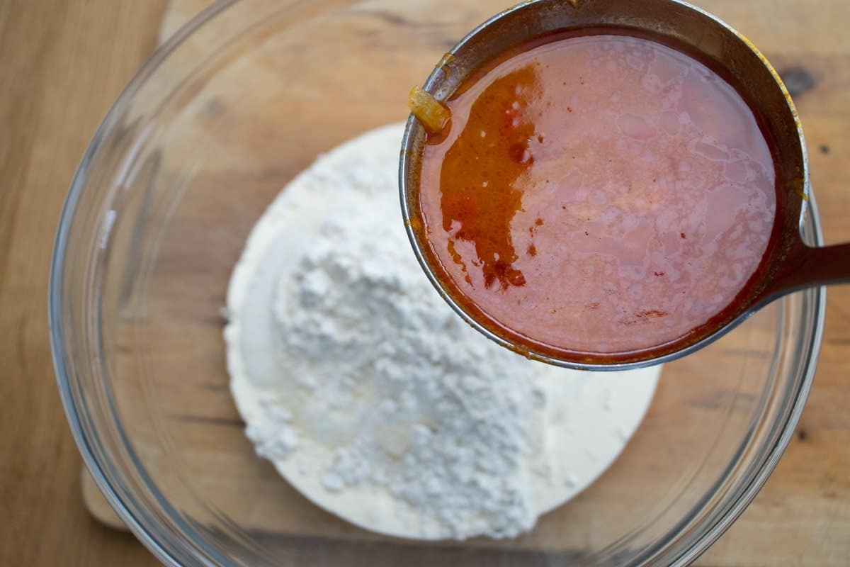 ladle with sauce from paprika chicken dish being held over sour cream and flour mixture in glass bowl