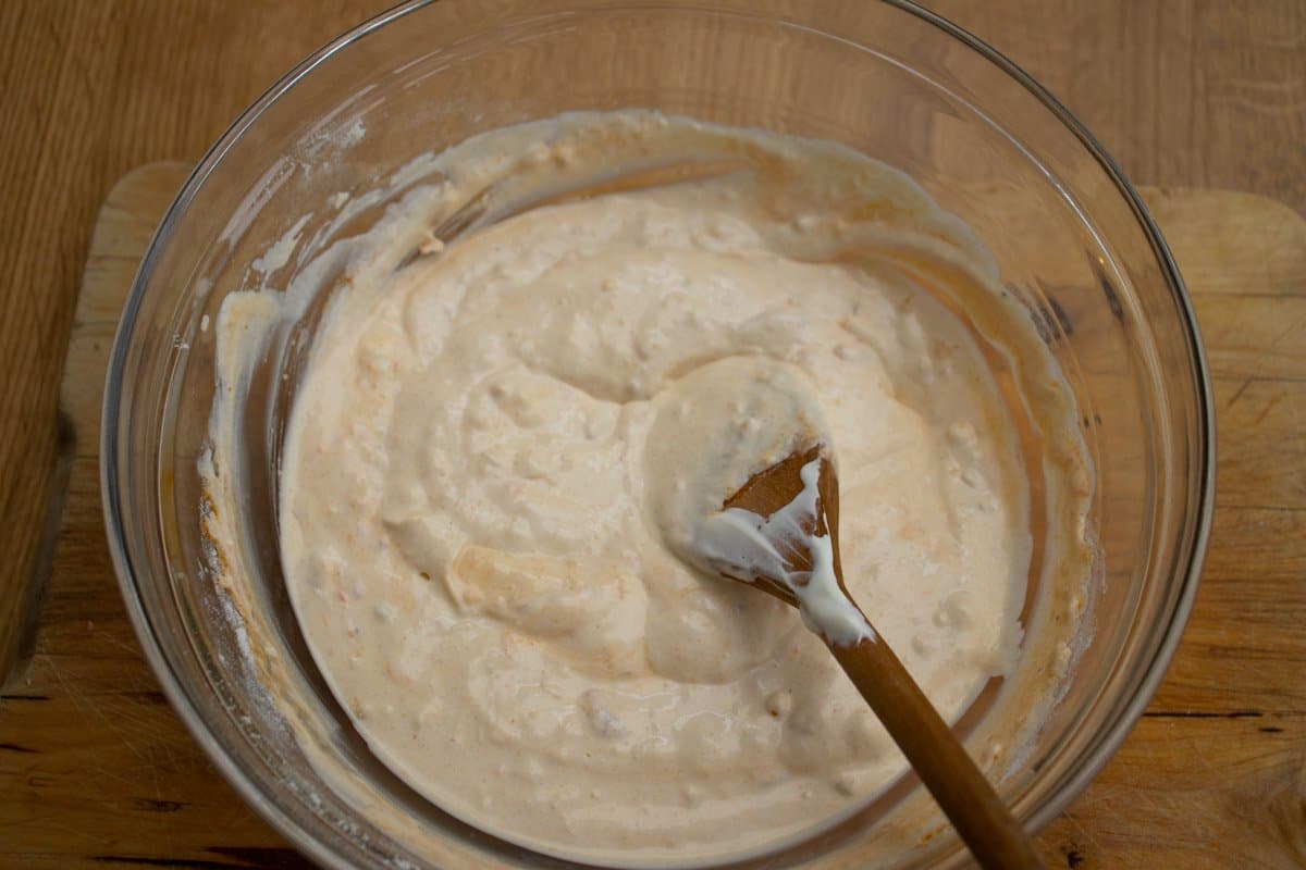 sour cream mixture in a glass mixing bowl being stirred with wooden spoon
