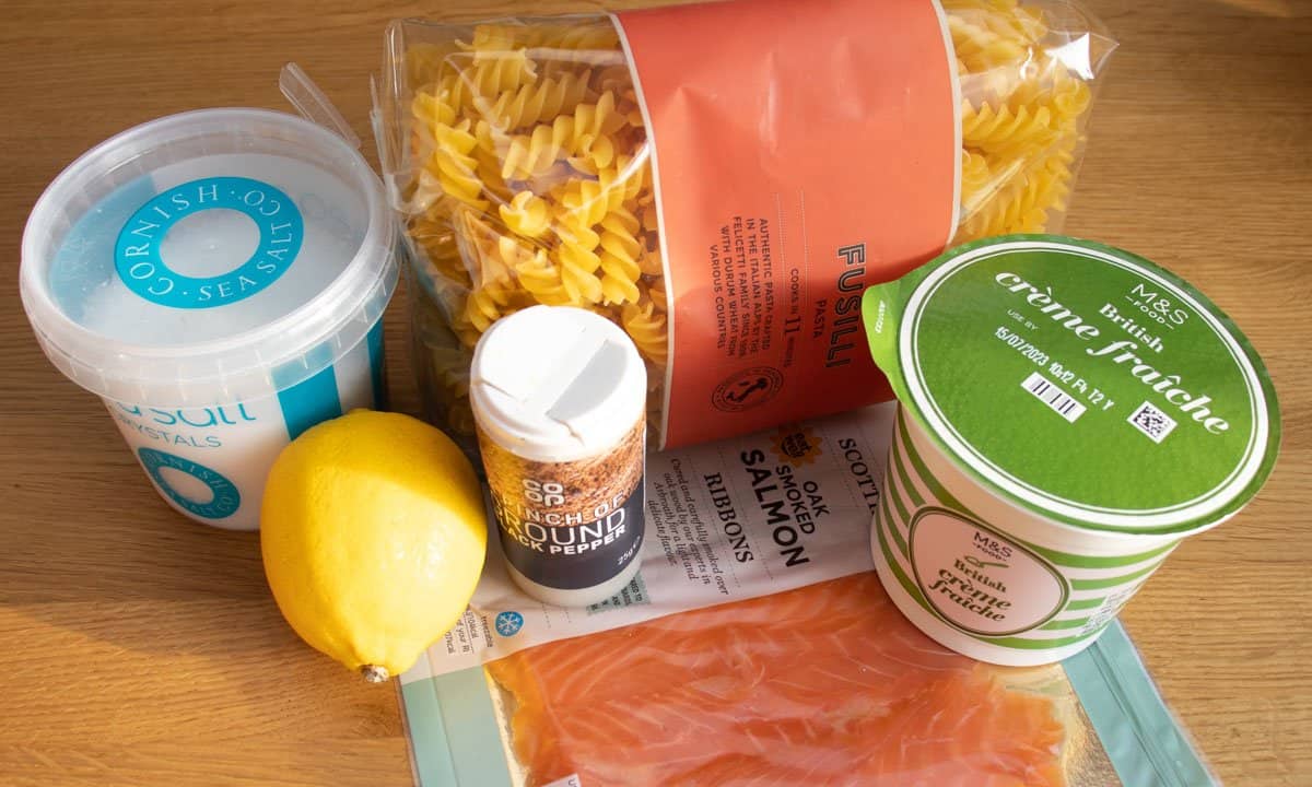 Salt, lemon, pepper, packet of fusilli pasta, packet of smoked salmon ribbons and tub of creme fraiche on wooden sideboard.