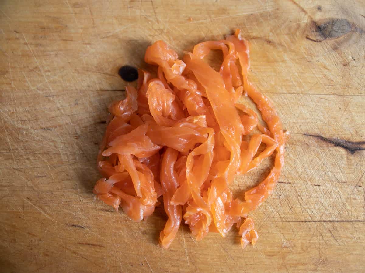 Smoked salmon cut into thin ribbons on wooden board.