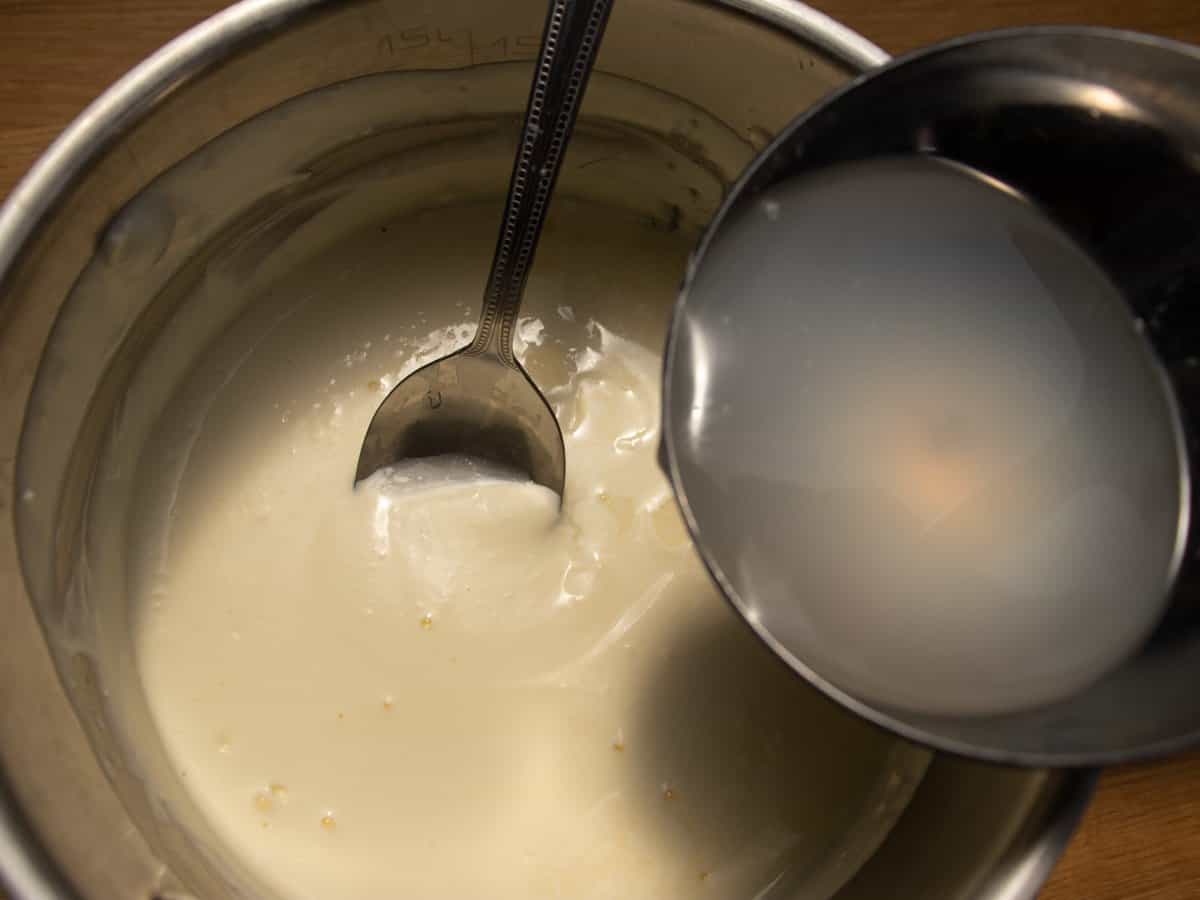 Creme fraiche mixture in a saucepan, ladle of pasta water being held over mixture.