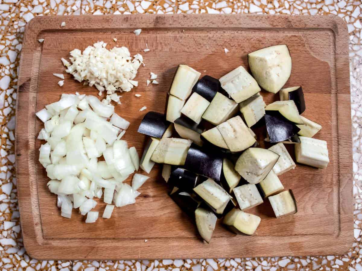 finely chopped garlic, finely chopped onion and aubergine cubes on a wooden board