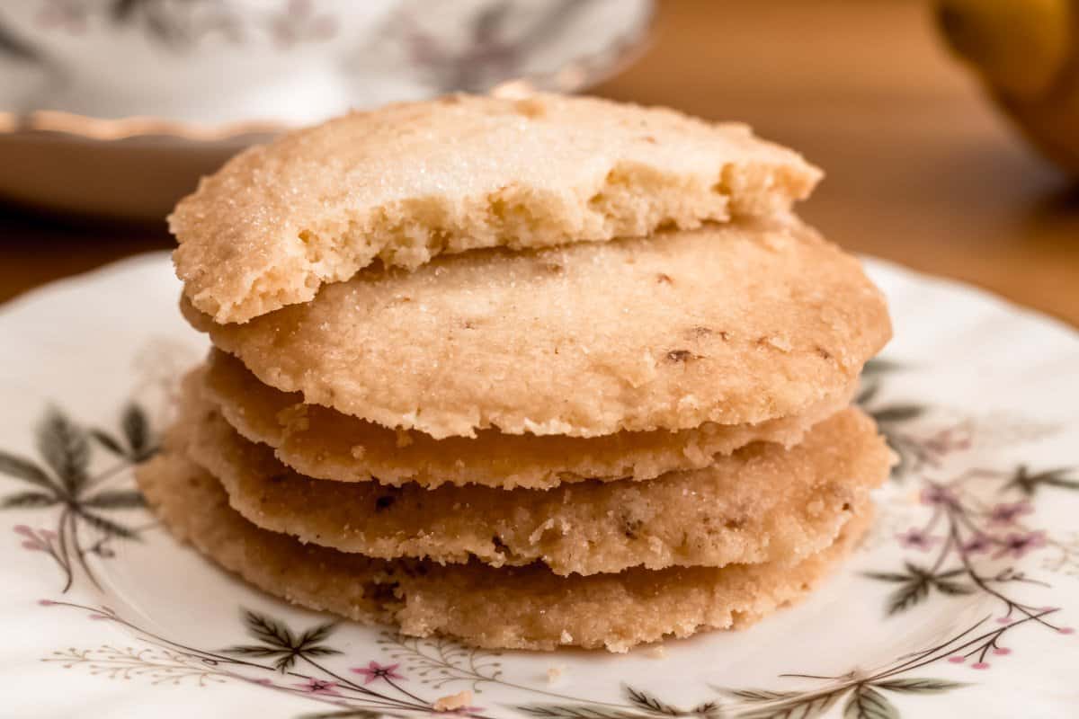 Pile of lemon butter biscuits on a saucer, top biscuit broken in half, teacup and saucer in background with lemon