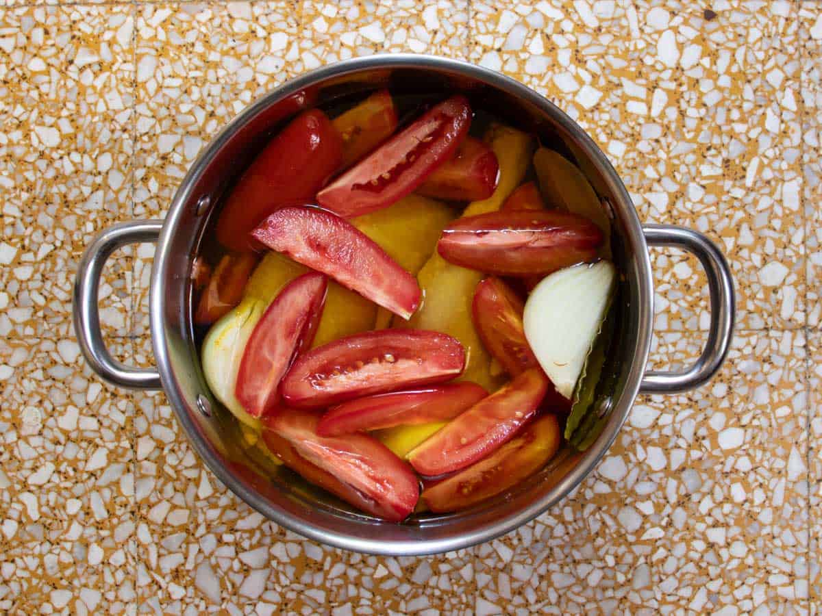 Sliced tomatoes, quartered onions, chicken pieces, bay leaf and other Cuban Chicken stock ingredients in water in saucepan.
