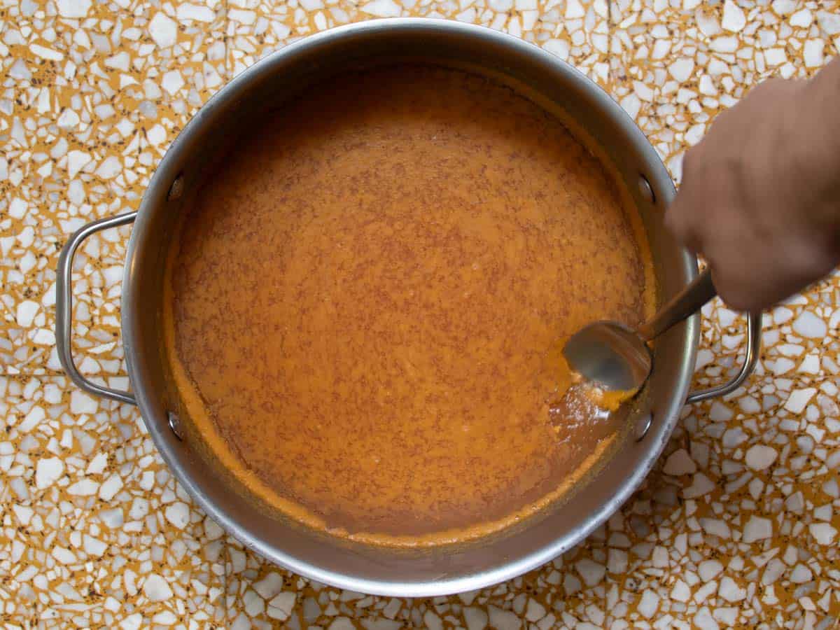 Cold Cuban chicken stock in stainless steel saucepan with the solidified fat at the surface of the stock being scooped out with a spoon.