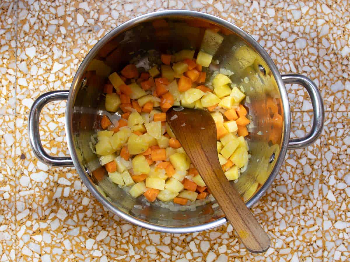 Diced potatoes, carrots and finely chopped onions lightly sweated in stainless steel saucepan with wooden stirring spoon.