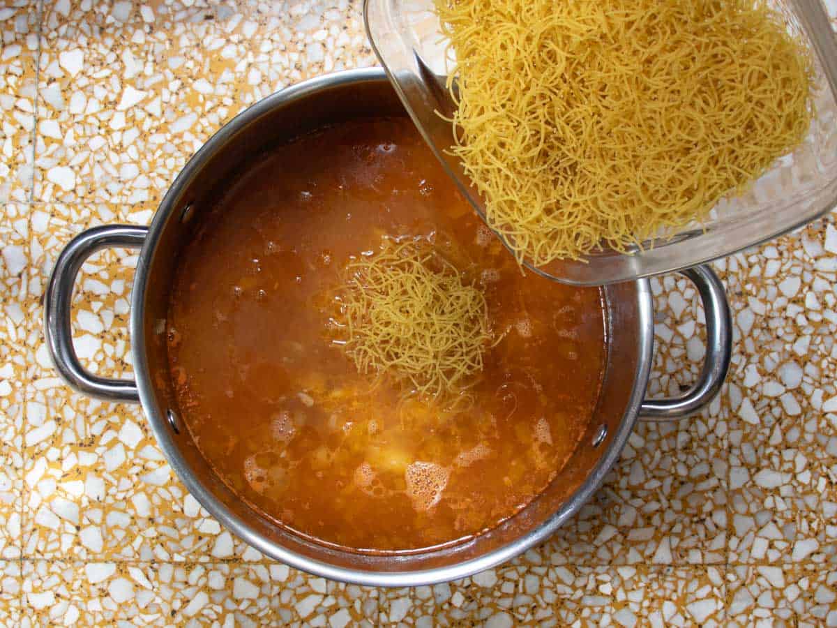 Vermicelli pasta being tipped into stainless steel saucepan containing Cuban Chicken stock.