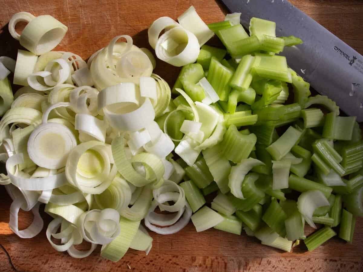 Chopped leeks and celery on board with chopping knife.