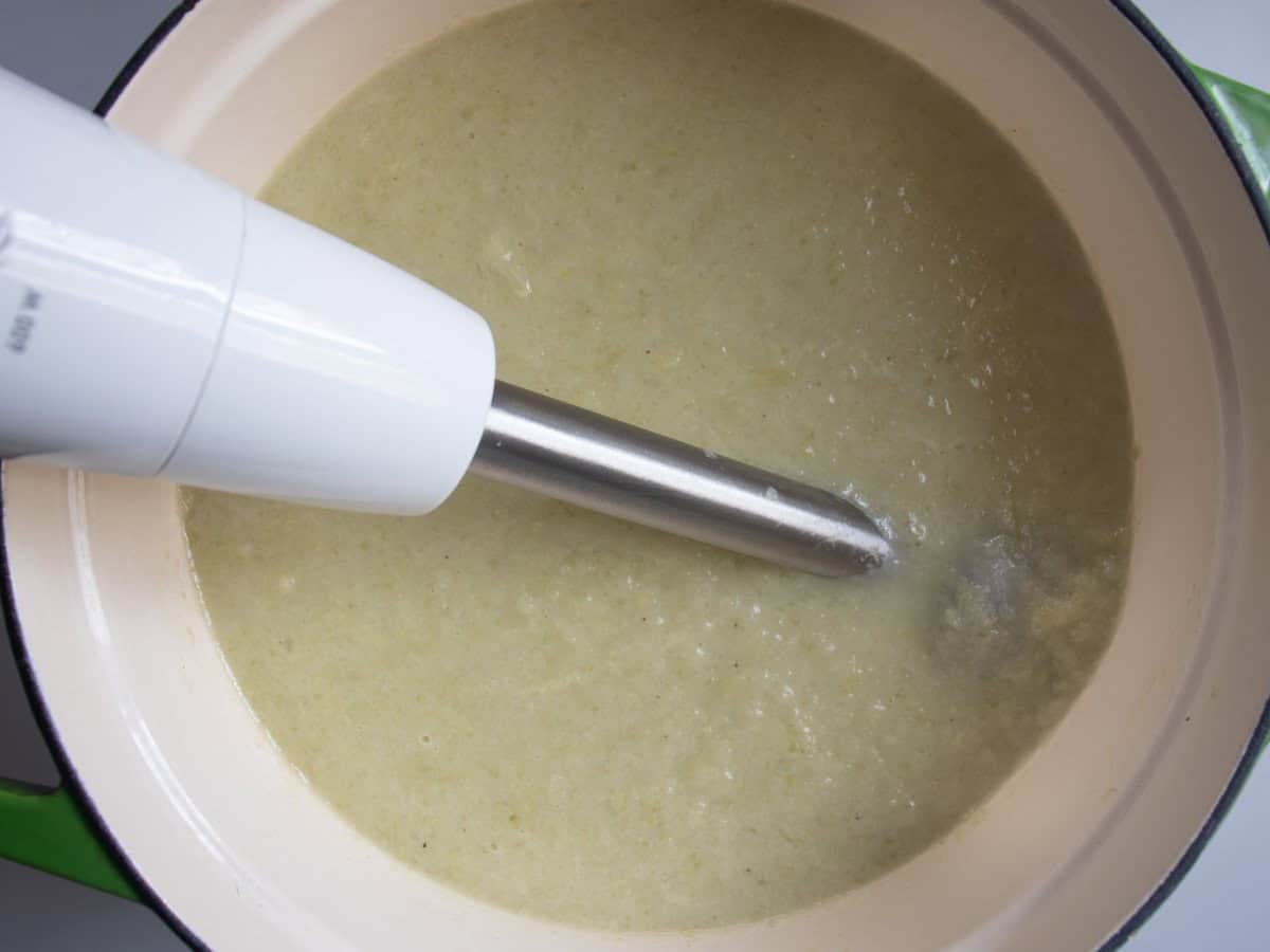 Blender in leek and celery soup in saucepan.