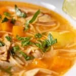 Cuban chicken noodle soup in a bowl sprinkled with chopped parsley and with a slice of lime on the side.