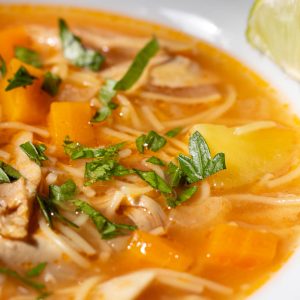 Cuban chicken noodle soup in a bowl sprinkled with chopped parsley and with a slice of lime on the side.