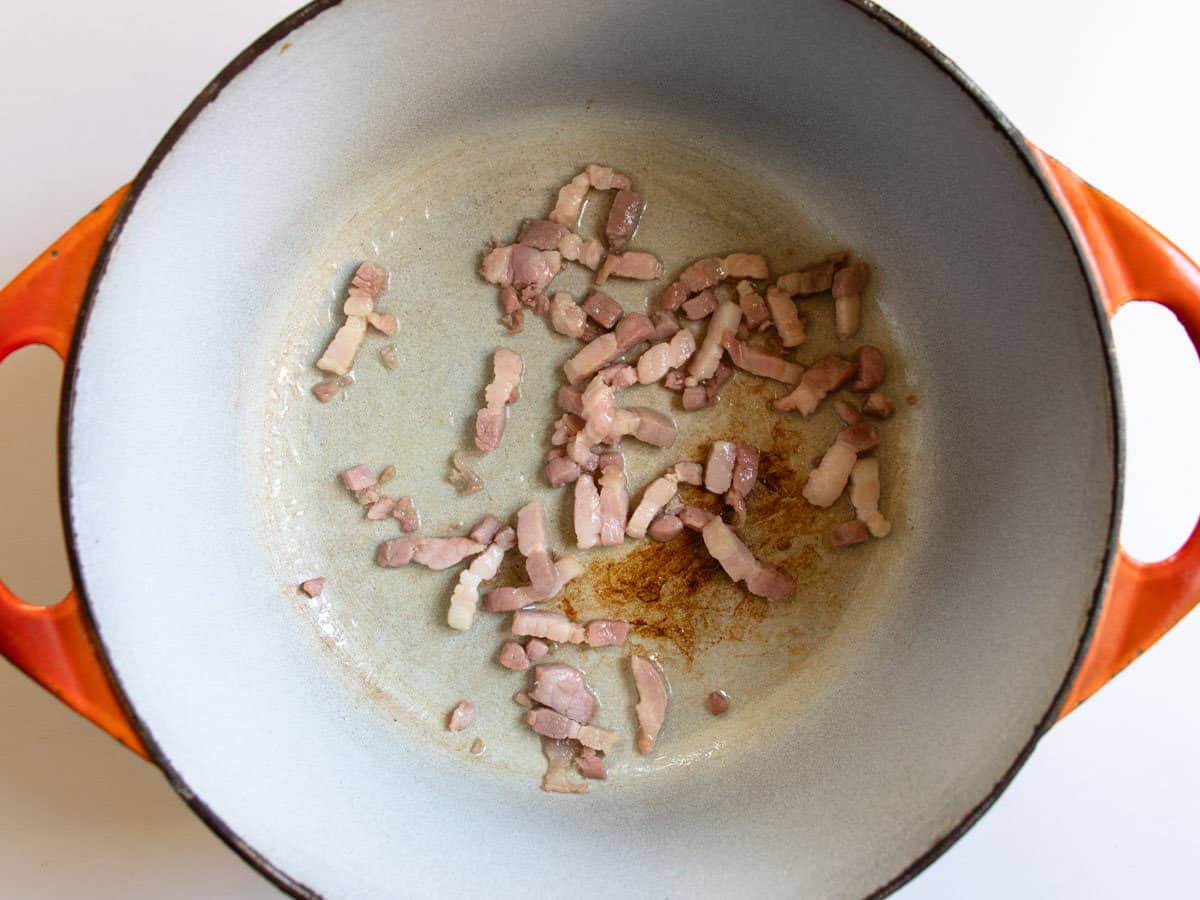 Lardons being fried in orange cast iron enamelled saucepan.