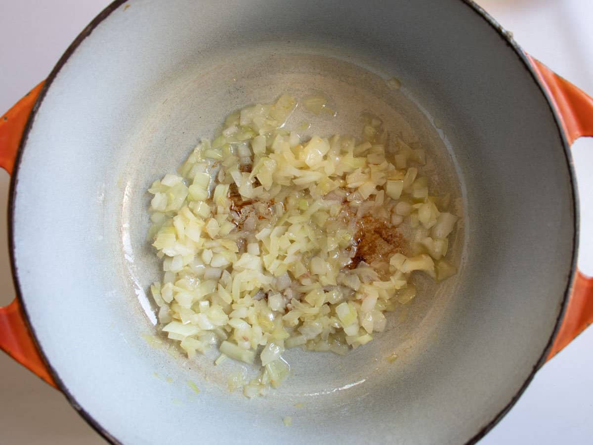 Finely chopped onion being fried in orange enamelled cast iron saucepan.