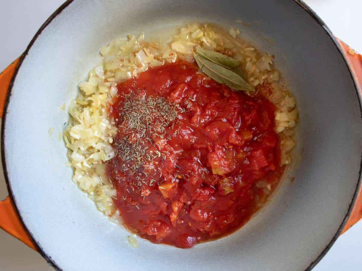 Fried onion, with chopped tinned tomatoes, dried thyme and bay leaves in saucepan.