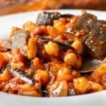 Close up of Lebanese Moussaka in a bowl with a spoon lifting up a spoonful of the chickpea mixture.