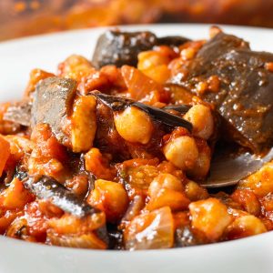 Close up of Lebanese Moussaka in a bowl with a spoon lifting up a spoonful of the chickpea mixture.