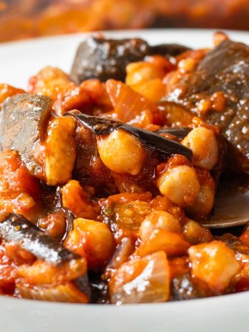 Close up of Lebanese Moussaka in a bowl with a spoon lifting up a spoonful of the chickpea mixture.