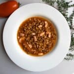French green lentil soup in white bowl next to sprig of fresh thyme and red tomato.