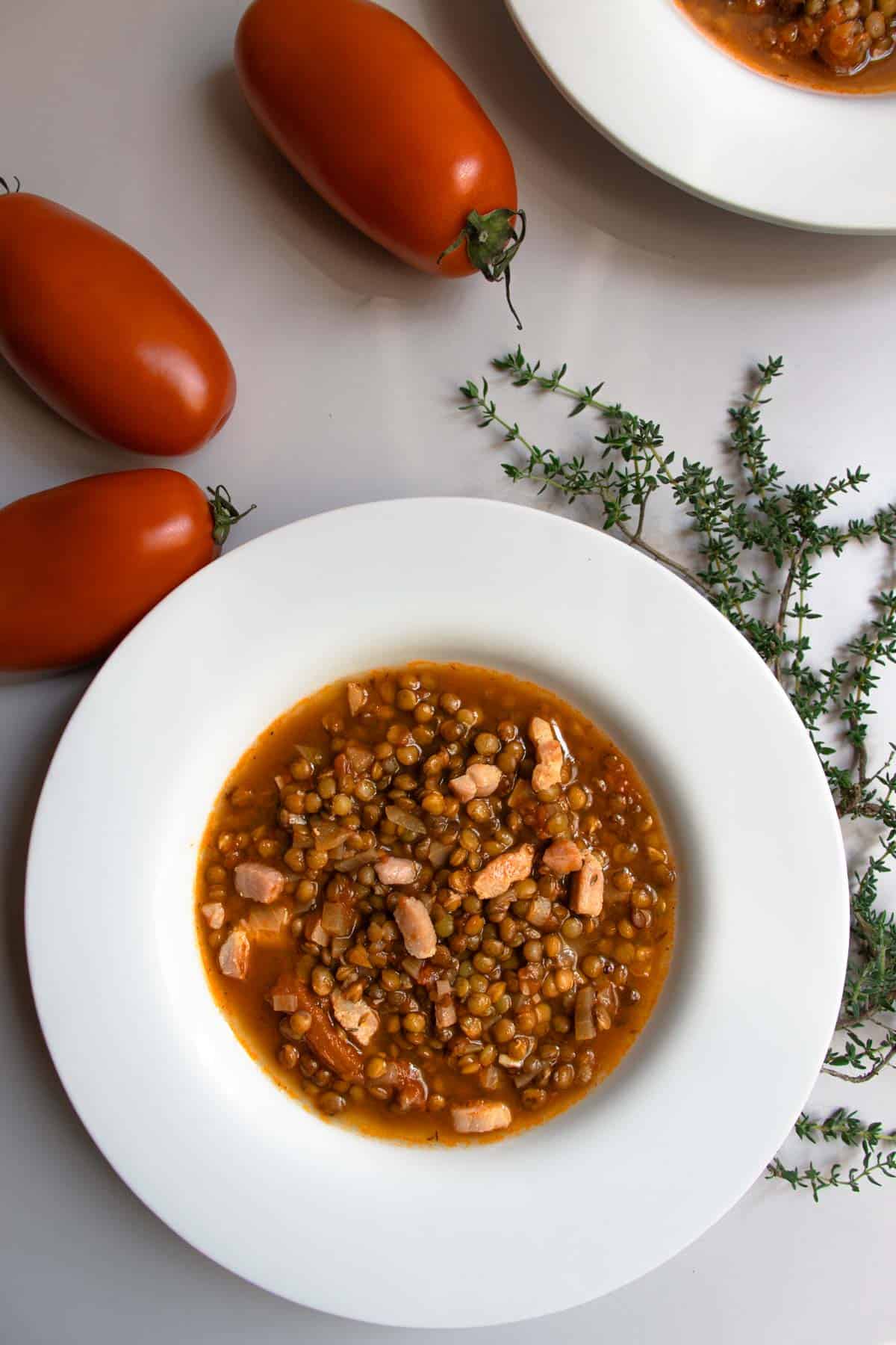 French green lentil soup in white bowls next to sprigs of fresh thyme and red tomatoes.