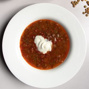 Hungarian lentil soup topped in centre with a dollop of soured cream in a white bowl next to a few scattered green lentils.
