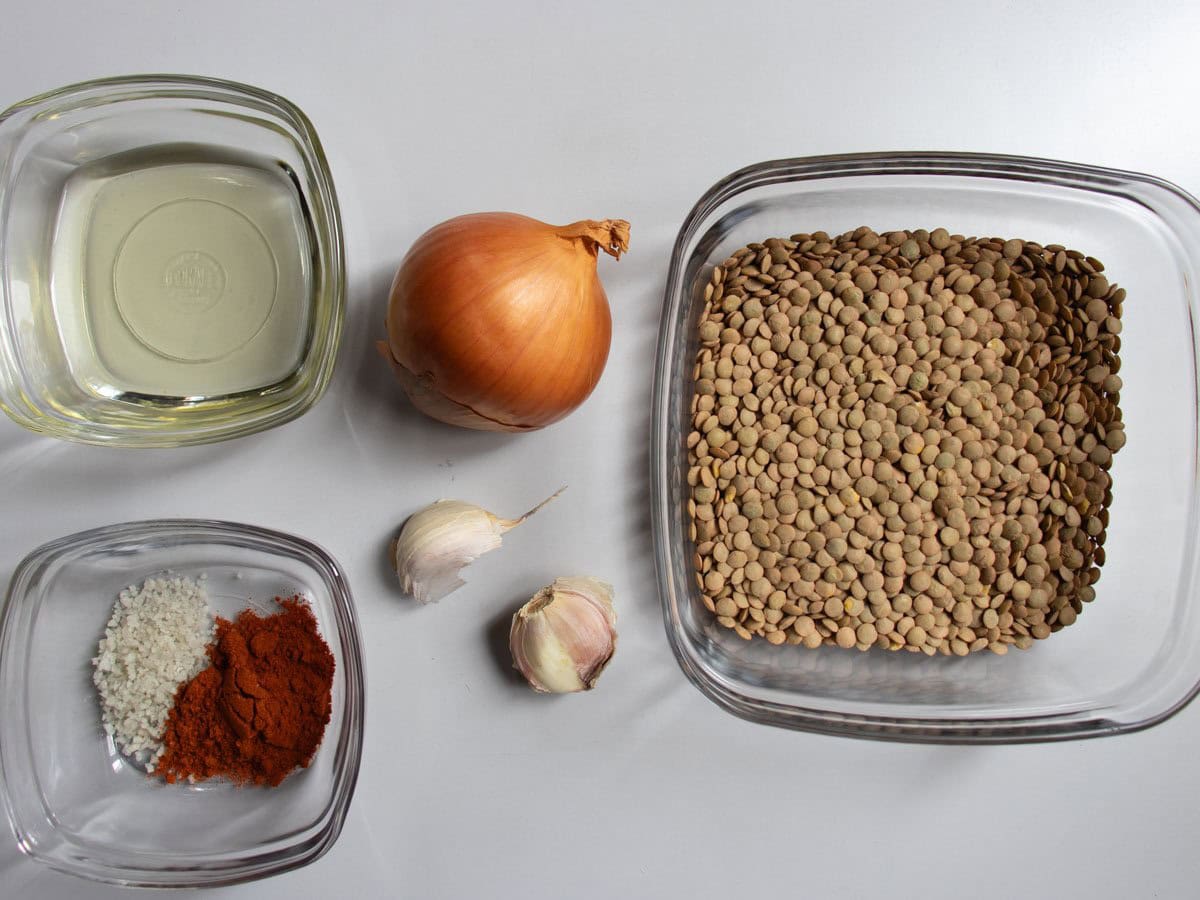 Ingredients for Hungarian lentil soup, onion, garlic cloves, green lentils (in glass bowl), oil (in glass bowl), salt and pepper (in glass bowl).