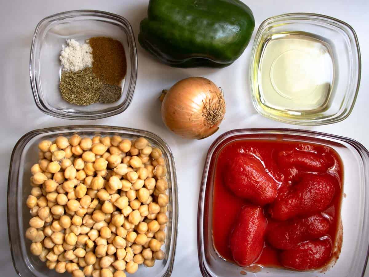 Ingredients for Chickpea and Tomato Soup with Peppers laid out in glass bowls on grey surface.