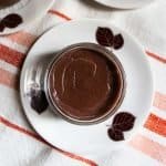 Chocolate crémeux pudding in small glass bowl on saucer with chocolate coloured leaves pattern, placed on orange red striped cloth.