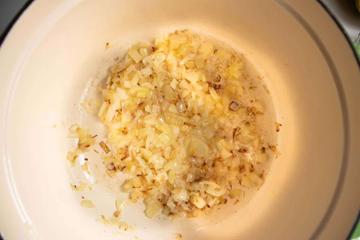 Finely chopped onion being fried in enamelled saucepan.