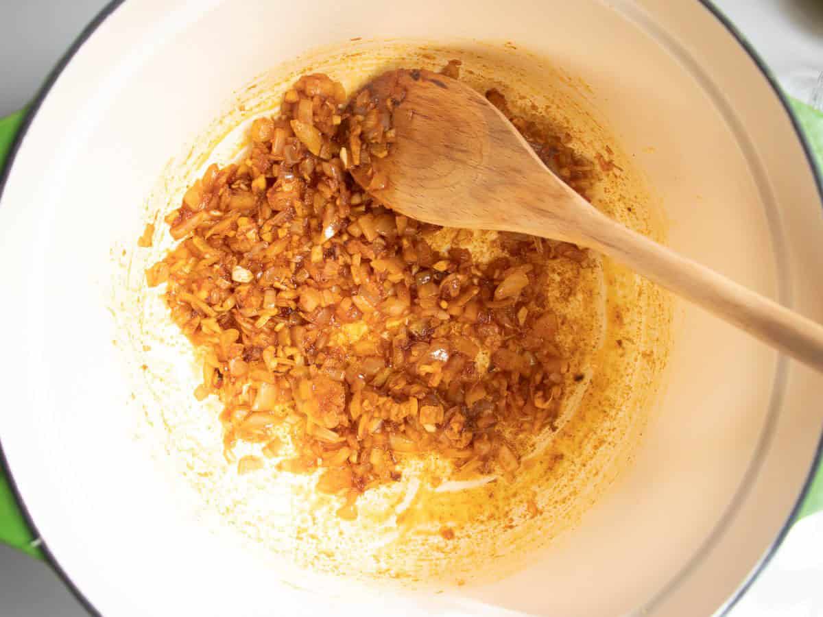Paprika being stirred into finely chopped onions and garlic in enamelled saucepan by wooden spoon.
