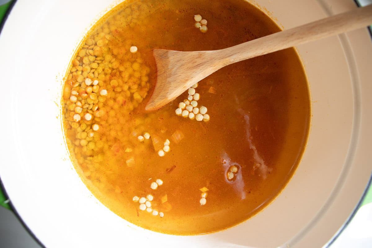 Uncooked lentils in water in an enamelled saucepan, being stirred by a wooden spoon,