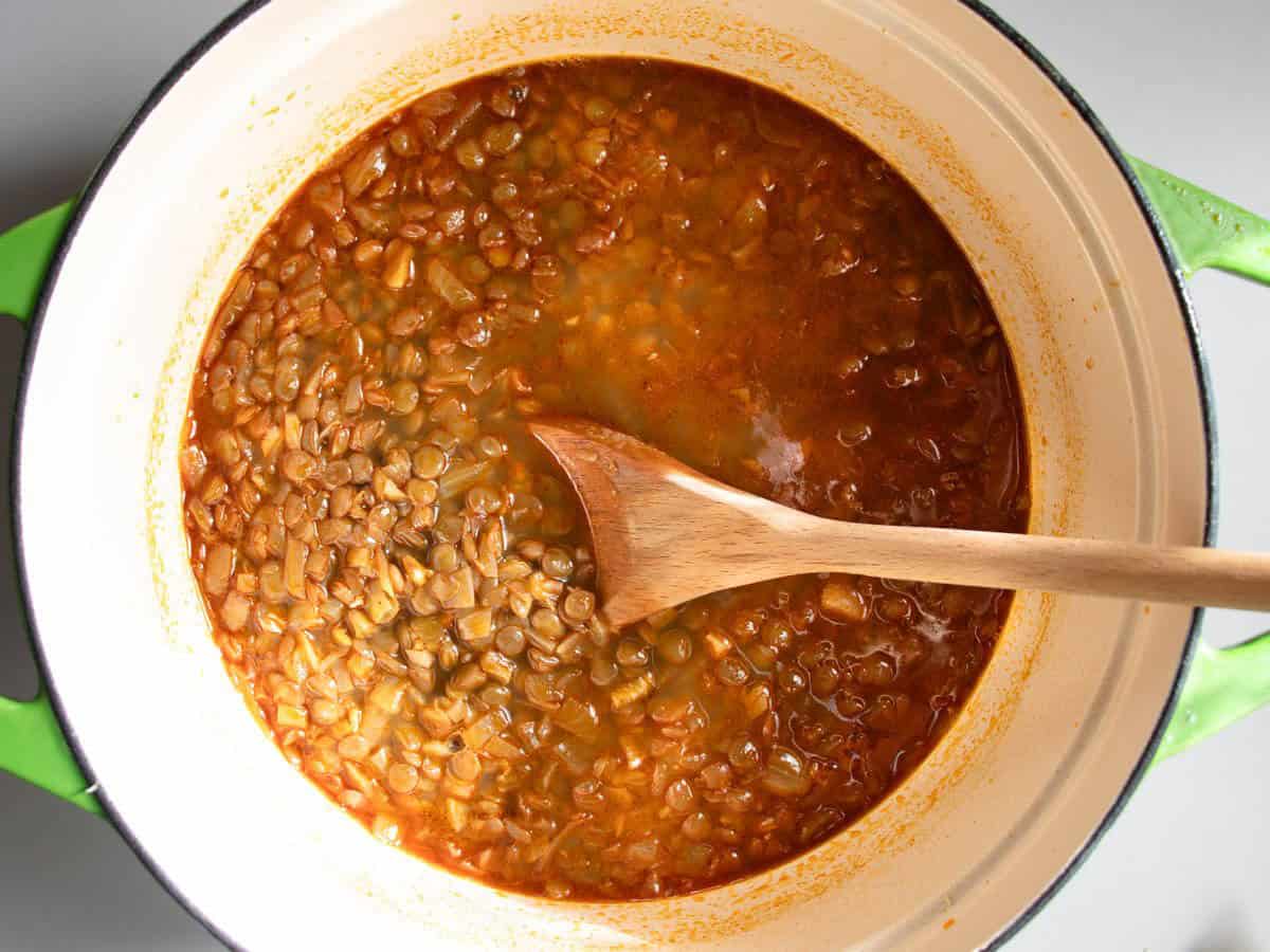 Hungarian lentil soup in an enamelled saucepan being stirred with a wooden spoon.